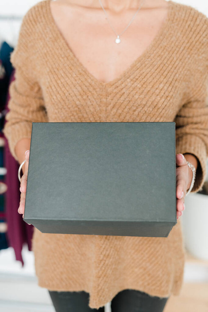 Černá krabička držená mladým příležitostným prodavačem nebo zákazníkem v béžovém pulovru stojící před kamerou - Fotografie, Obrázek