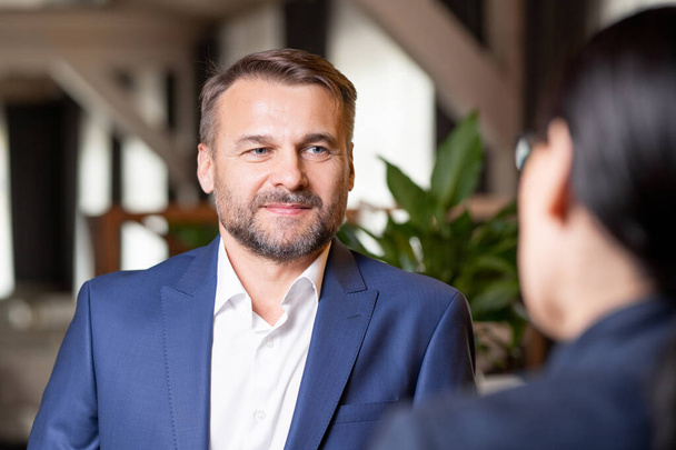 Happy bearded businessman in elegant suit having discussion with colleague at working meeting in restaurant - Фото, зображення