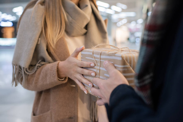 Bej renkli yün ceketli genç bir kadının elleri kocasının ya da erkek arkadaşının önünde dururken hediye kutusunu alıyor. - Fotoğraf, Görsel