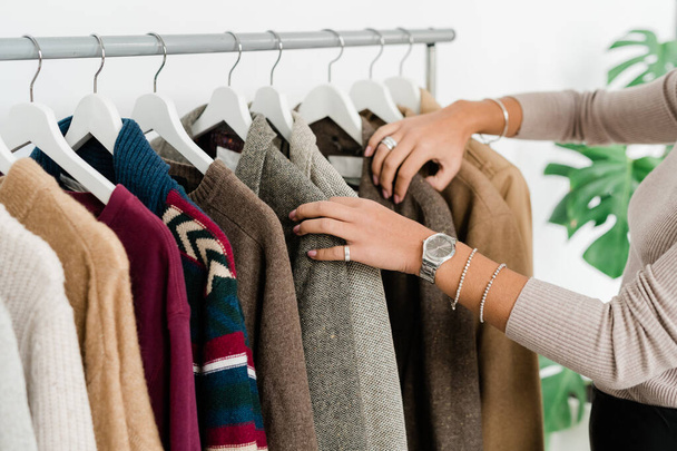Casual joven hembra adicta a las compras de pie por fila de ropa nueva y elegante al elegir chaqueta o suéter
 - Foto, Imagen