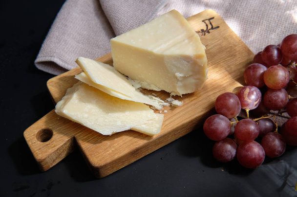 Pieces of parmigiano reggiano or parmesan cheese on wood board on dark background - Photo, image