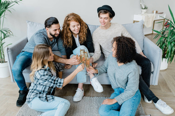 Cinco jóvenes amigos alegres en ropa de casualwear tintineo con flautas de champán mientras se celebran las vacaciones en casa
 - Foto, imagen