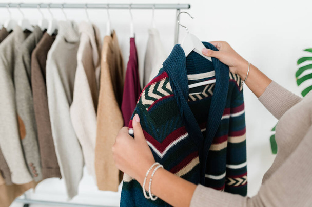 Jeune femme tenant un cintre avec un nouveau cardigan tricoté chaud tout en choisissant des vêtements de la collection saisonnière
 - Photo, image