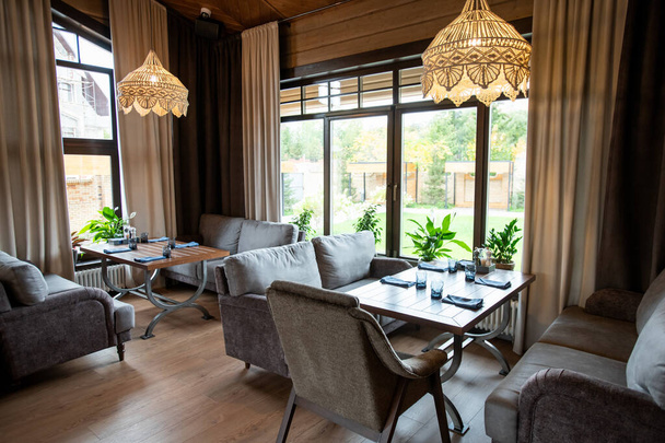 Декоративные люстры, висящие на потолке над обслуживаемыми столами и удобными диванами в уютном ресторане
 - Фото, изображение