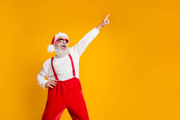 Portrait of funny crazy santa claus hipster in red hat fun christmas x-mas party celebrate newyear time dance raise index finger wear shirt suspenders isolated yellow color background - Foto, imagen