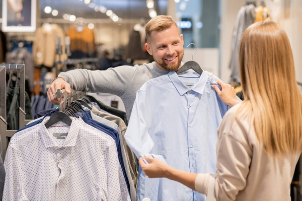 Młoda para wybiera nową koszulę dla mężczyzny stojąc przy stoliku z nową kolekcją w dziale odzieżowym w centrum handlowym - Zdjęcie, obraz