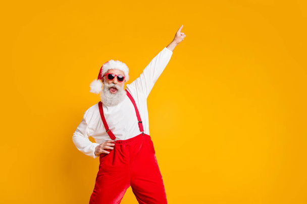 Christmas party hard. Portrait of crazy funny santa claus hipster in red hat enjoy x-mas noel celebration dance raise index finger wear shirt suspenders isolated yellow color background - Photo, Image