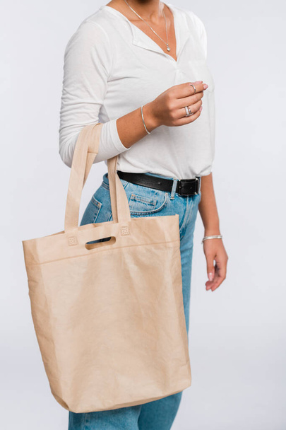 Young casual woman in white polo shirt and blue jeans carrying big shopping bag in isolation - Fotoğraf, Görsel