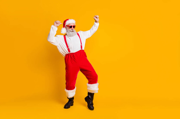 Full length photo of grey hair cool funny santa claus in red x-mas hat enjoy newyear christmas magic tradition celebration dance wear shirt suspenders boots isolated yellow color background - Foto, immagini
