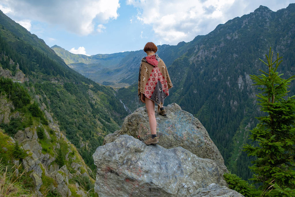 Joven viajera vestida con un poncho de pie en las hermosas montañas
  - Foto, imagen