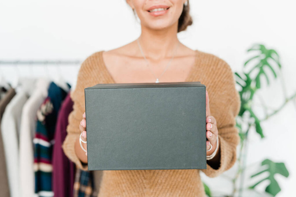 Caja negra en manos de un joven asistente de tienda sonriente dándotelo o sosteniéndote frente a la cámara en la boutique
 - Foto, imagen