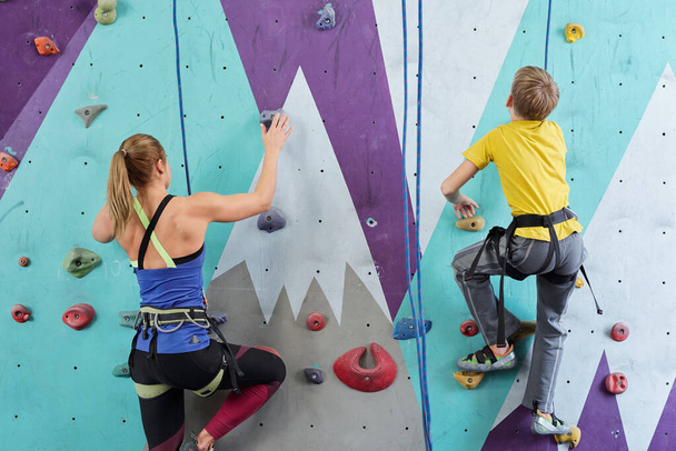 Vista posterior del colegial y la joven en ropa deportiva agarrando por pequeñas rocas en la pared de escalada durante el entrenamiento deportivo
 - Foto, imagen