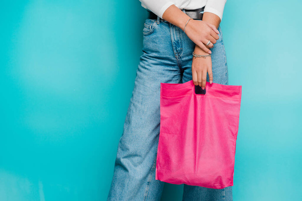 Onderste deel van jonge casual vrouwelijke shopper in blauwe jeans houden fucsia roze textiel shopping tas - Foto, afbeelding