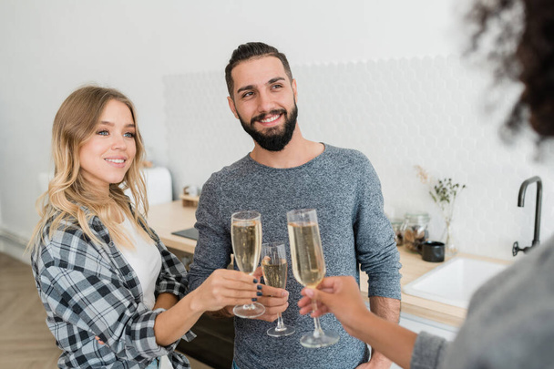 Szczęśliwa młoda para z fletem szampana toasting z jednym z ich przyjaciół w domu party - Zdjęcie, obraz