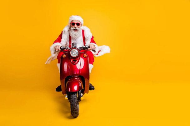 Full length photo of crazy funky santa claus in red hat drive motorcycle ride fast hurry to x-mas noel celebration wear shirt suspenders isolated over yellow color background - Foto, imagen