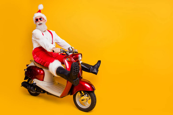 Full body photo of funny santa white hair grandpa rushing newyear party speed retro bike wear trendy sun specs red trousers cap shirt boots isolated yellow color background - Фото, зображення