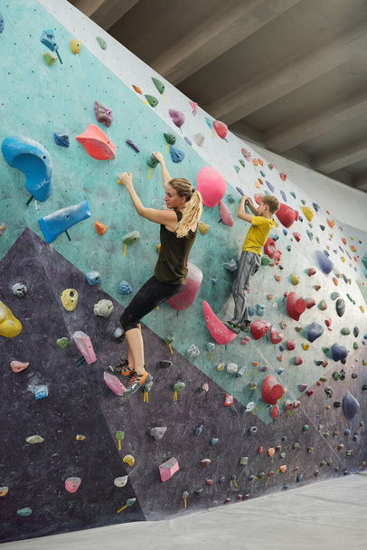 Jeune femme blonde active et son fils en vêtements de sport mur d'escalade avec de petites roches artificielles tout en s'entraînant à loisir
 - Photo, image