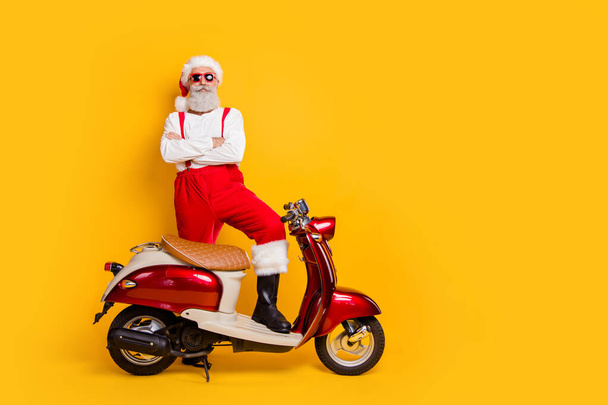 Full length photo of santa arrogant man standing self-confident near retro moped bike crossed arms wear trendy sun specs pants cap shirt isolated yellow color background - Photo, Image