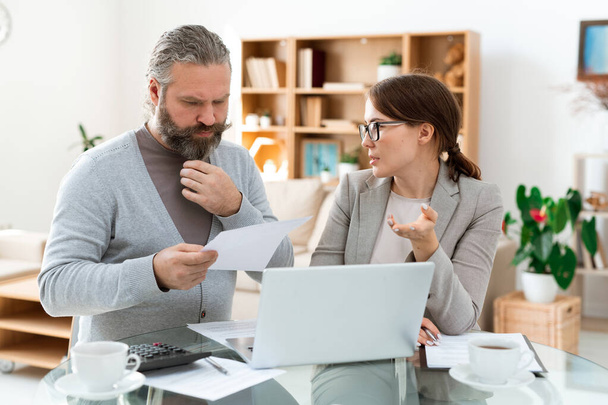 Homme barbu pensif avec les cheveux gris regardant à travers le papier tout en écoutant son agent immobilier à la réunion
 - Photo, image