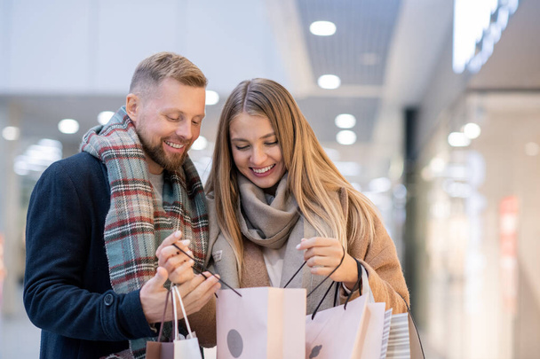 Jóvenes adictos a las compras con bolsas de papel mirando lo que compraron en la venta de temporada en el centro comercial
 - Foto, Imagen