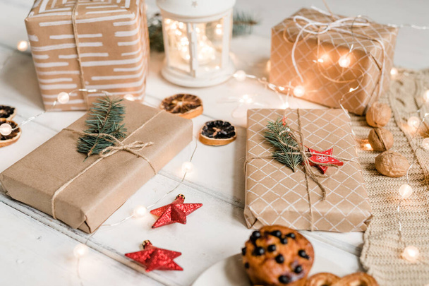 Több csomagolt ajándék között dekoratív vörös csillagok, dió, csillogó koszorúk, citrom szeletek és cookie-k fehér asztalon - Fotó, kép