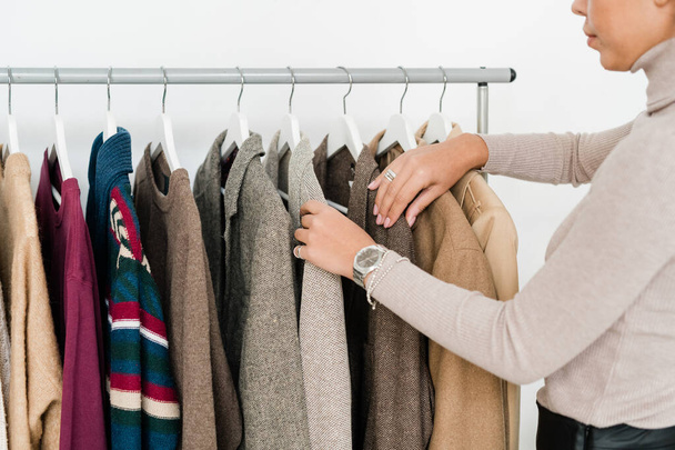 Молодая случайная женщина просматривает новую сезонную коллекцию одежды, стоя у стойки в бутике
 - Фото, изображение