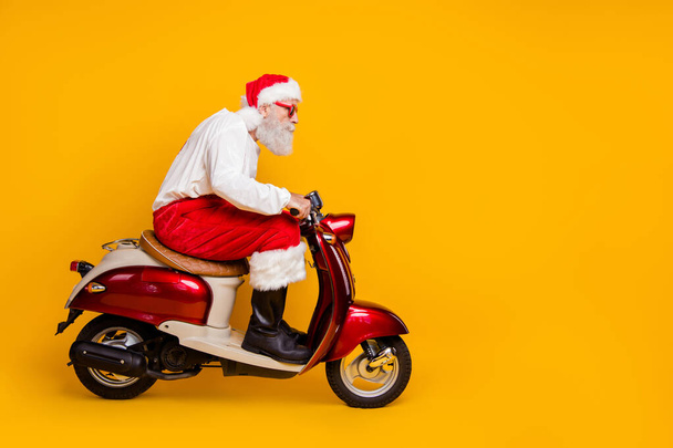 Full body profile photo of santa white hair grandpa riding speed x-mas theme party by bike wear trendy sun specs trousers cap shirt boots isolated yellow color background - Foto, Bild