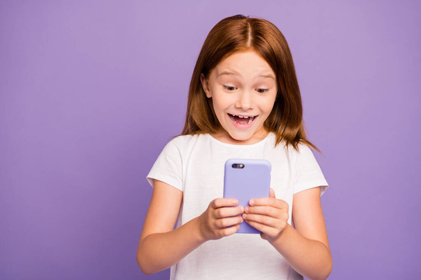 Photo of pretty small foxy lady holding telephone hands checking children blog excited with many new followers subscribers wear white t-shirt isolated purple background - Foto, Imagen