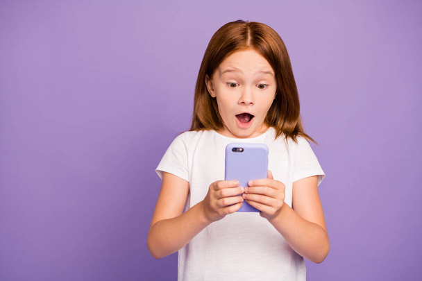 Foto von hübschen kleinen Ingwerdame hält Telefon Hände prüfen eigenen Kinder Blog begeistert mit vielen neuen Followern tragen weißes T-Shirt isoliert lila Hintergrund - Foto, Bild