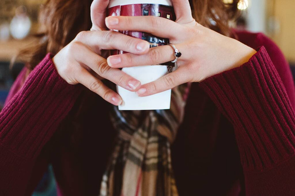 Closeup shot of a female drinking her coffee with two hands with a blurred background - Valokuva, kuva