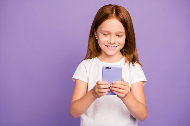 Photo of pretty little ginger lady holding telephone hands reading blog post interesting children useful information wear white t-shirt isolated purple background - Foto, Bild