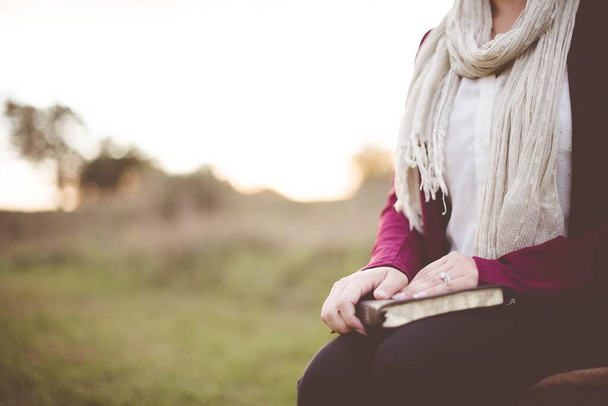 Closeup shot of a female sitting while holding the bible with a blurred background - Foto, Imagen