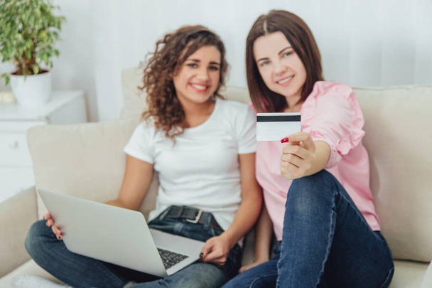 Blurred happy female friends sitting on the sofa using laptop and credit card for shopping online. - Fotografie, Obrázek