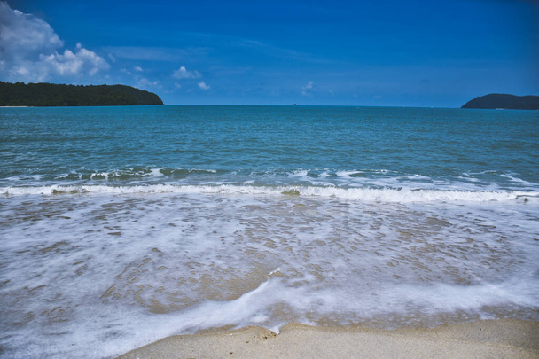 Ondas do mar azul de Andamão sob o céu azul atingindo as margens da bela praia de areia exótica e deslumbrante Cenang na ilha Langkawi, na Malásia
 - Foto, Imagem