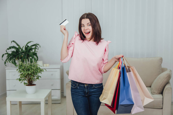 Young caucasian girl is standing with a lot of bags from shop and credit card in her hands, looking at the camera with excited face expression. - Foto, Bild