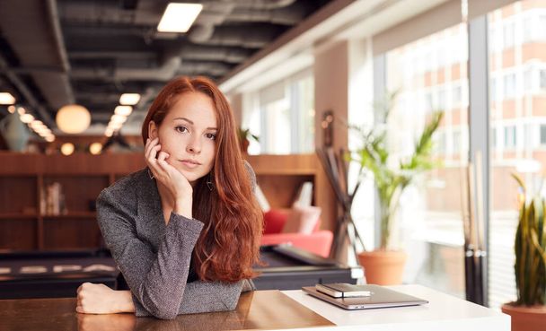 Portret van casual geklede jonge zakenvrouw werken aan bureau in moderne open werkplaats - Foto, afbeelding