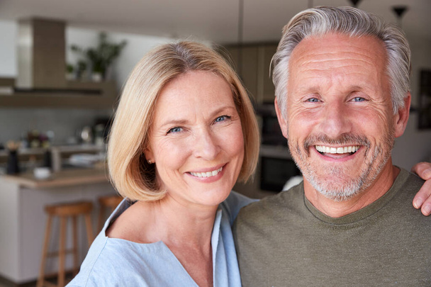 Portrait Of Smiling Senior Couple Standing At Home In Kitchen Together - Valokuva, kuva