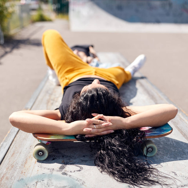 Young Woman Lying On Skateboard In Urban Skate Park - Фото, изображение