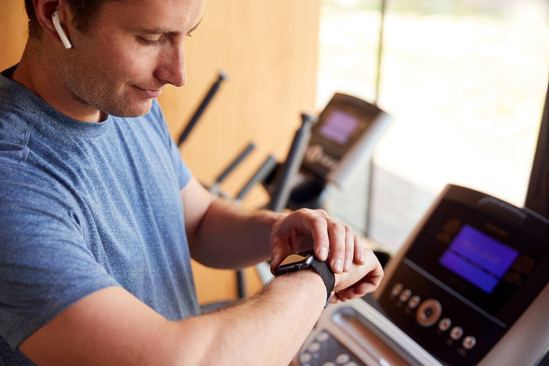 Мужчина упражняется на беговой дорожке дома носить беспроводные наушники Проверка Smart Watch
 - Фото, изображение