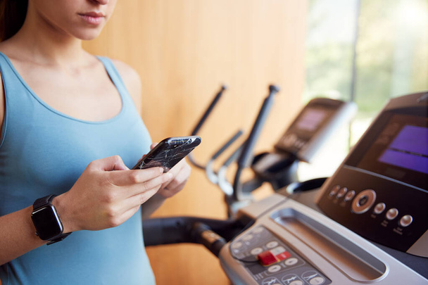 Close Up Of Woman Exercising On Treadmill Wearing Smart Watch Checking Mobile Phone - Zdjęcie, obraz