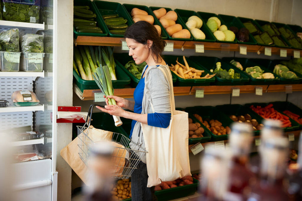 Female Customer With Shopping Basket Buying Fresh Leeks In Organic Farm Shop - Foto, Imagem