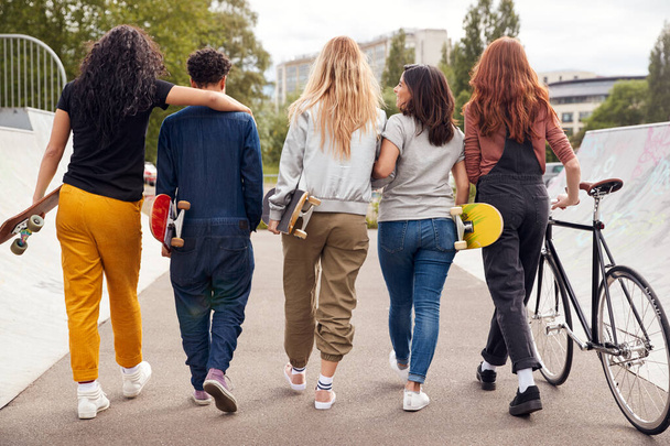 Rear View Of Female Friends With Skateboards And Bike Walking Through Urban Skate Park - Φωτογραφία, εικόνα