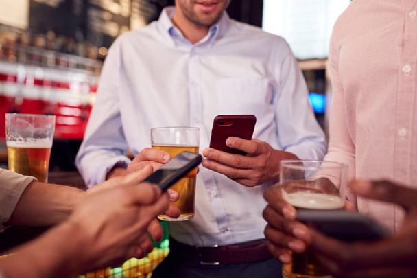 Group Of Male Friends All Checking Mobile Phones Whilst Meeting For Drink In Bar - Foto, Imagem