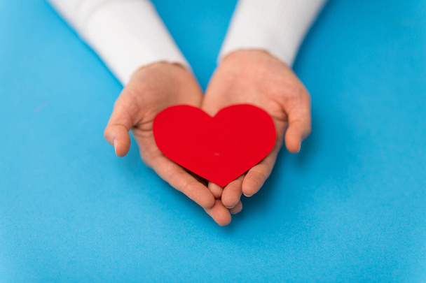 hands holding red heart shape on blue background - 写真・画像