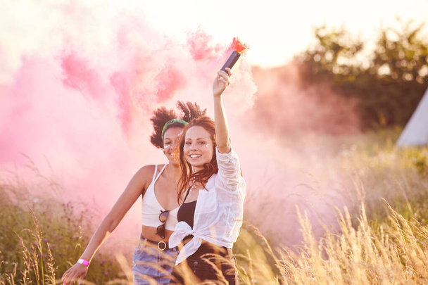 Deux femmes amis Camping au festival de musique Courir à travers le champ avec Smoke Flare
 - Photo, image