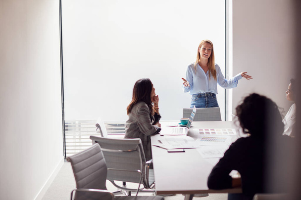 Female Boss Gives Presentation To Team Of Young Businesswomen Meeting Around Table In Modern Office - 写真・画像