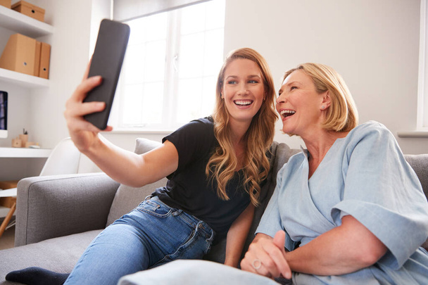Senior Mother With Adult Daughter Sitting On Sofa Posing For Selfie On Mobile Phone - Foto, Imagem
