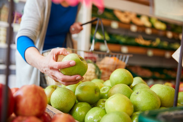 Κοντινό πλάνο του πελάτη γυναίκα με καλάθι αγορά φρέσκα μήλα σε κατάστημα βιολογικών γεωργικών προϊόντων - Φωτογραφία, εικόνα