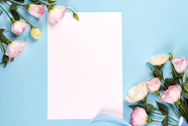 Composição do quadro com espaço vazio no papel central feito de eustoma rosa florescente, flat lay. cantos decorativos florais no fundo azul
. - Foto, Imagem