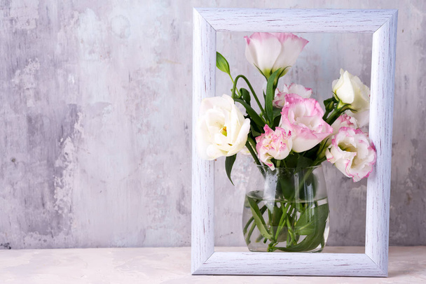 Eustoma flowers in vase in photo frame on table near stone wall, space for text. Blank for postcards - Photo, Image